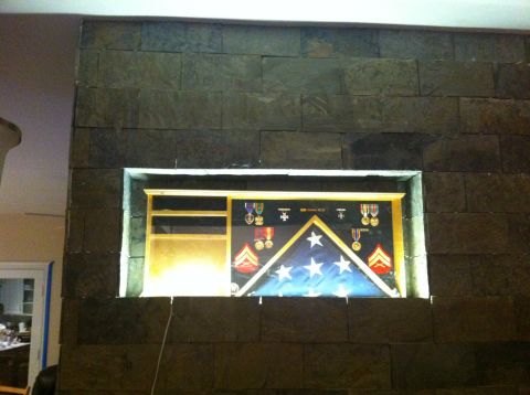 1989 Yugo Cabrio - A display case containing a folded American flag and various military medals is mounted on a stone wall.
