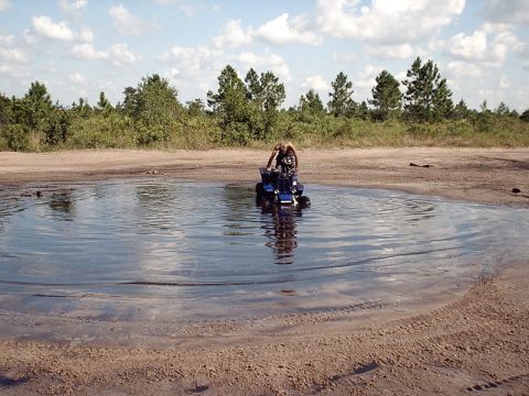 1996 Ford Bronco - ATV rider navigates a muddy water obstacle on a sunny day.
