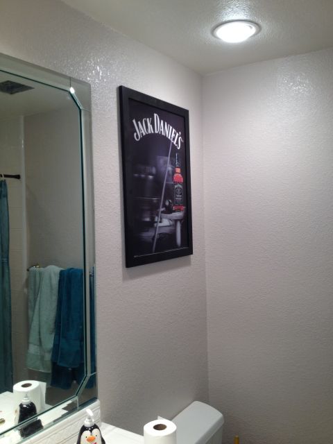 1989 Yugo Cabrio - A framed Jack Daniel's advertisement hangs on a textured wall in a bathroom, next to a mirror and shower.