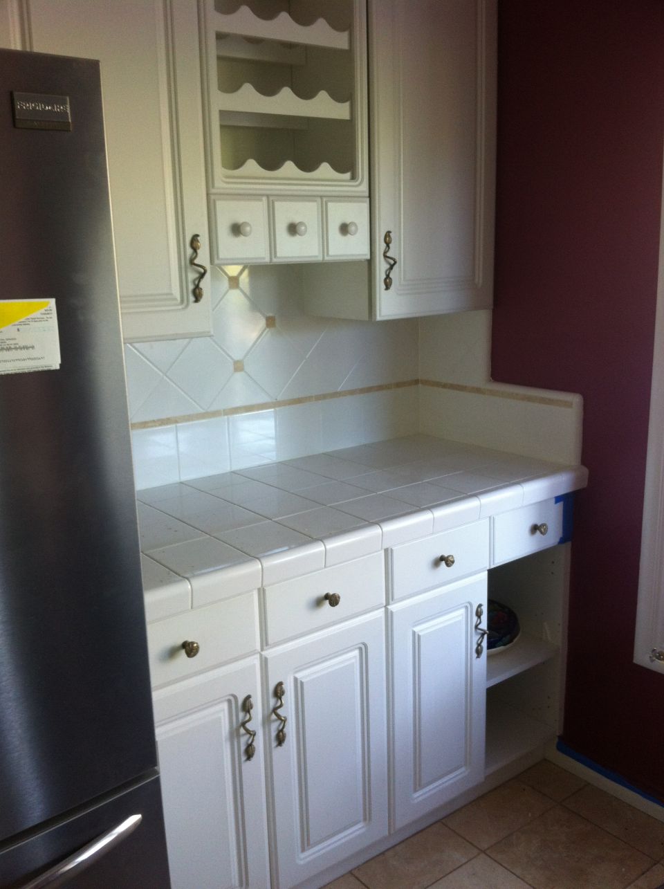 White kitchen cabinets with tiled countertop and a stainless steel refrigerator