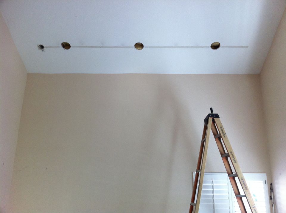 Wooden A-frame ladder positioned in front of a window with blinds, near a ceiling with four circular openings