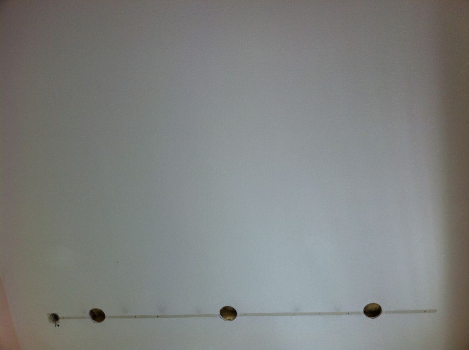 Wall with four holes and a thin metal strip running horizontally across them. Supermotors.net logo in lower right