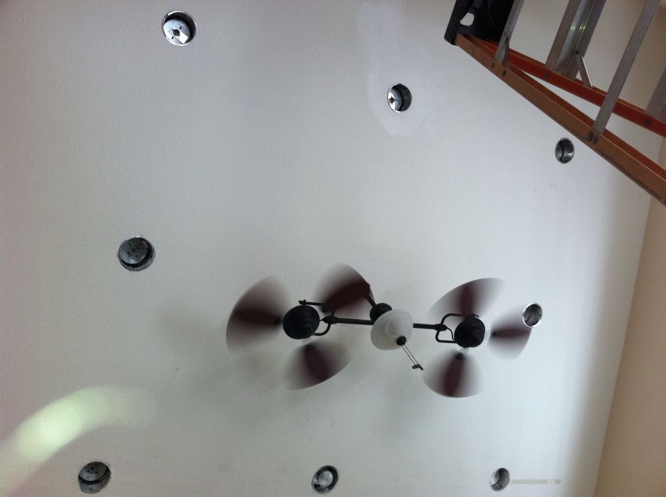 Ceiling fan with four blades, overhead view. Ladder in background