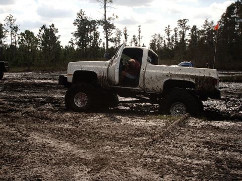 1996 Ford Bronco - A white pickup truck is stuck in the mud with its driver inside.