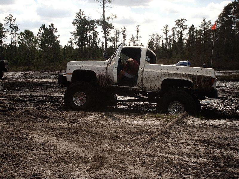 White lifted mud-covered pickup in muddy off-road field, side view