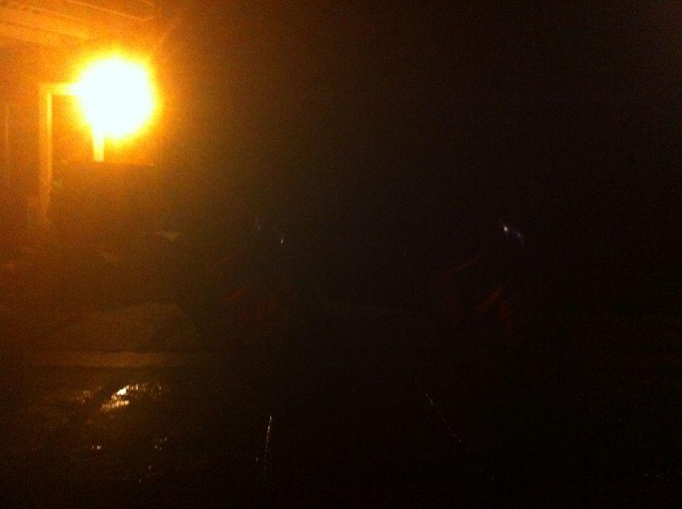 Dark scene with a car silhouette under a bright light, wet ground