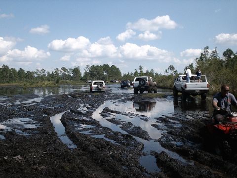 1996 Ford Bronco - Off-road vehicles navigate a challenging muddy track under a partly cloudy sky.