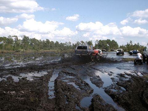 1996 Ford Bronco - Off-road vehicles navigate a challenging muddy terrain under a partly cloudy sky.