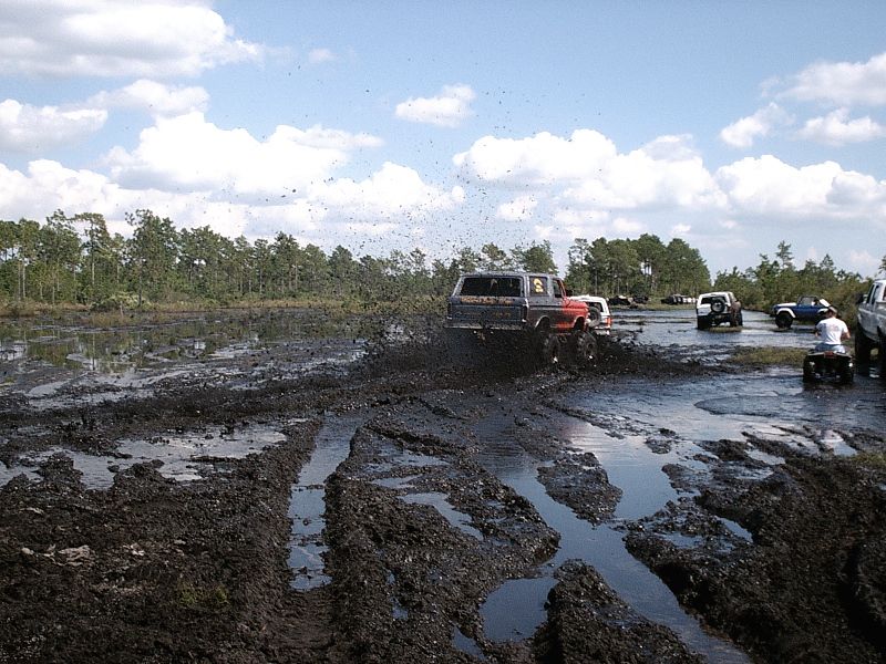 Dark Bronco with red lower body throwing mud in a bog with other 4x4s watching