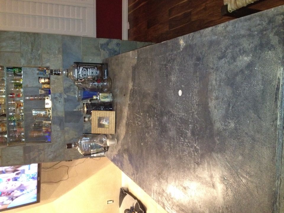 Bar with shelves of bottles, a TV, and a dark countertop