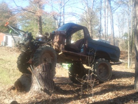 1978 Ford Bronco - This heavily modified 1978 Ford Bronco sits on a tree stump, its front end showing significant damage and exposed engine components.