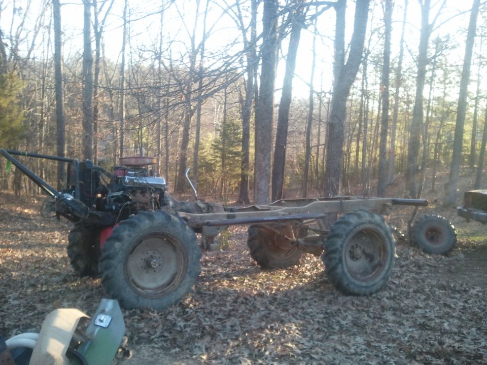 Chassis with large tires and engine in wooded area. Another tire visible