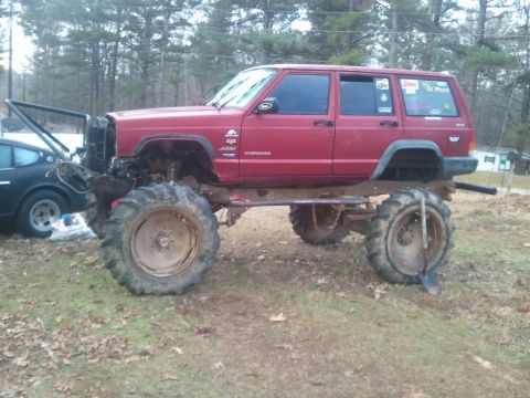 1978 Ford Bronco - Modified Jeep Cherokee with oversized tires sits in a grassy area next to another vehicle.