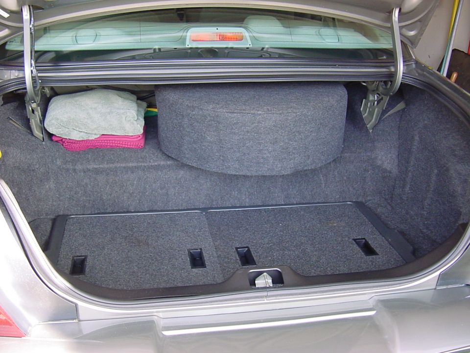 Open trunk of a gray sedan with dark carpet, a round carpeted enclosure, and folded towels
