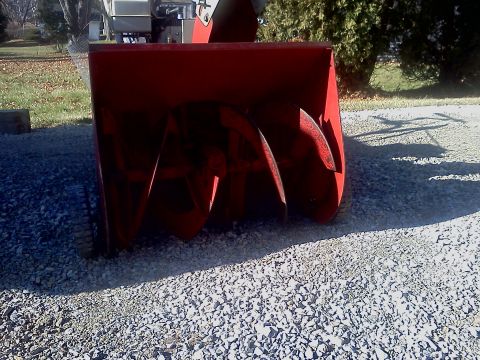 1991 Toyota Tacoma - Close-up of a red snow blower auger mechanism on a gravel surface.