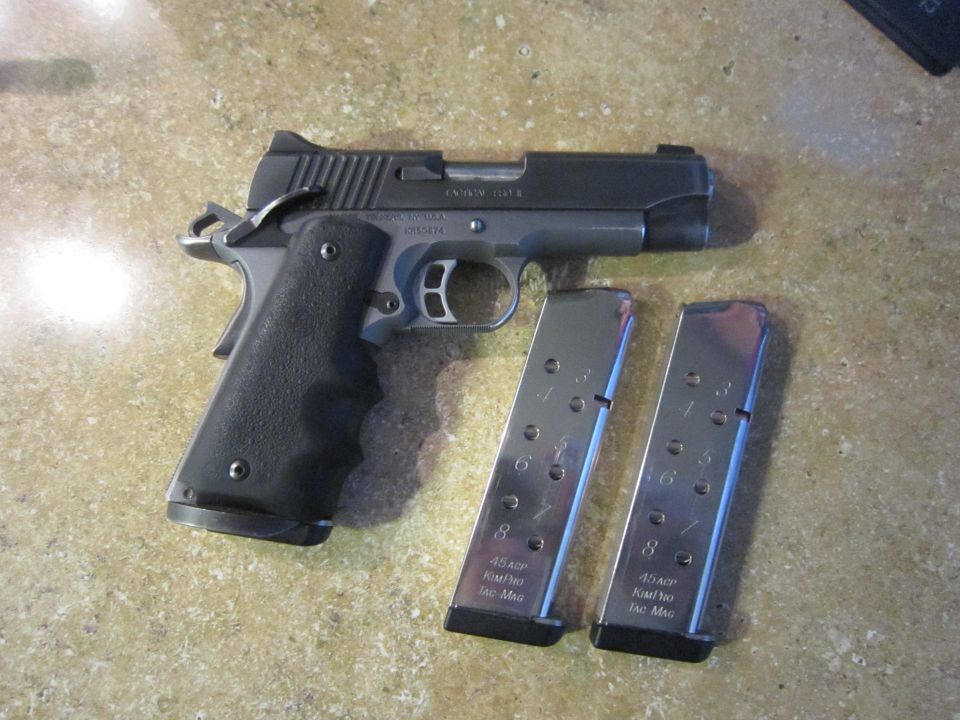 Two-tone pistol with black grip and two chrome magazines on a speckled surface