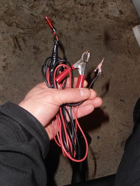 1990 Ford Bronco - A hand holds a set of jumper cables, complete with red and black wires and alligator clips, ready for use.