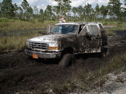 1996 Ford Bronco - Mud-covered 1996 Ford Bronco stuck in a muddy field with grass and trees in the background.