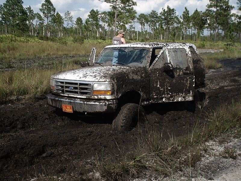 Mud-covered Ford SUV stuck in a mud bog with a person at the open driver's door