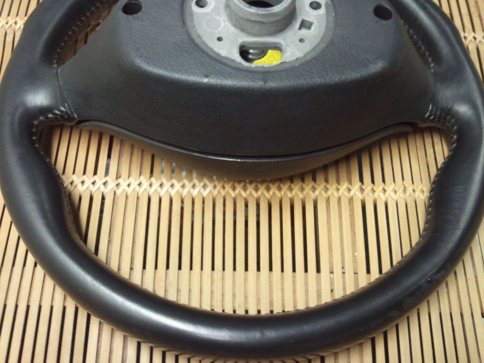 Black leather steering wheel with metal hub, on a bamboo mat