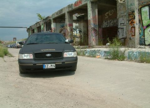 2003 Ford Crown Victoria - A Ford Crown Victoria, possibly a police interceptor, is parked in front of an abandoned, graffiti-covered structure.