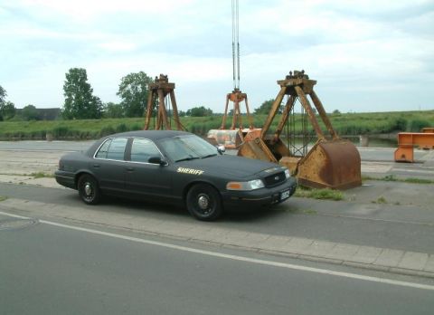 2003 Ford Crown Victoria - A black Ford Crown Victoria police car is parked outdoors near large industrial cranes.