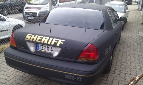 2003 Ford Crown Victoria - A black Ford Crown Victoria, marked as a Sheriff vehicle, is parked in a lot with other cars and vans.