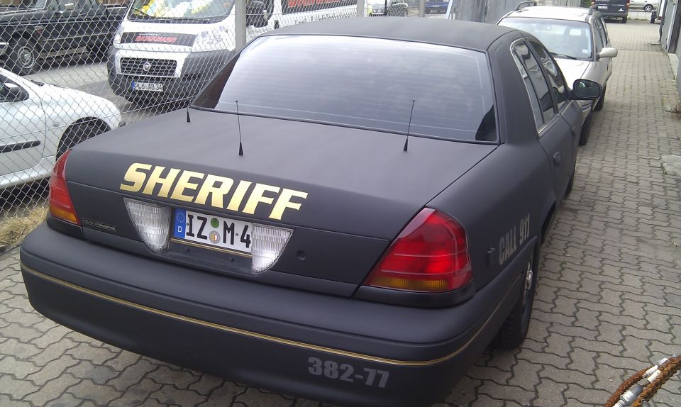 Black Ford Crown Victoria with 'SHERIFF' in gold on the trunk, parked next to other vehicles