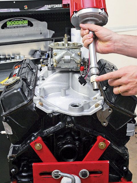 1990 Ford Bronco - A person is installing a distributor into a V8 engine, which is mounted on an engine stand.