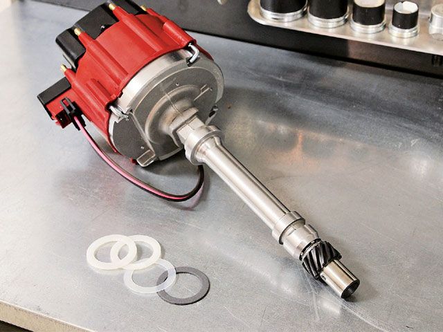 Red and silver distributor cap with wires and gaskets on a metal surface