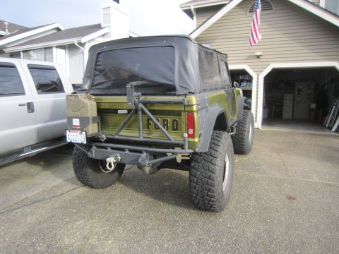 1974 Ford Bronco - A modified Ford Bronco is parked in front of a garage, with a silver pickup truck beside it.