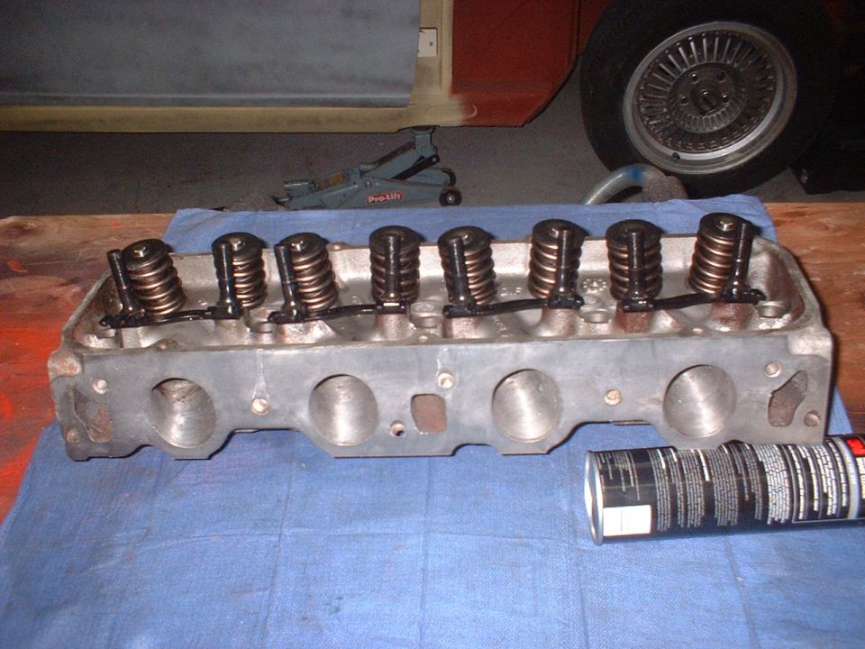 Engine cylinder head with valves and springs, can of spray lubricant on blue cloth