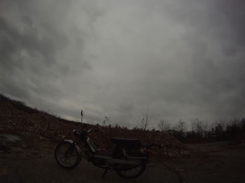 1981 Garelli Rally Sport - A moped sits parked on a dirt path, with a rocky hill and bare trees in the background under an overcast sky.