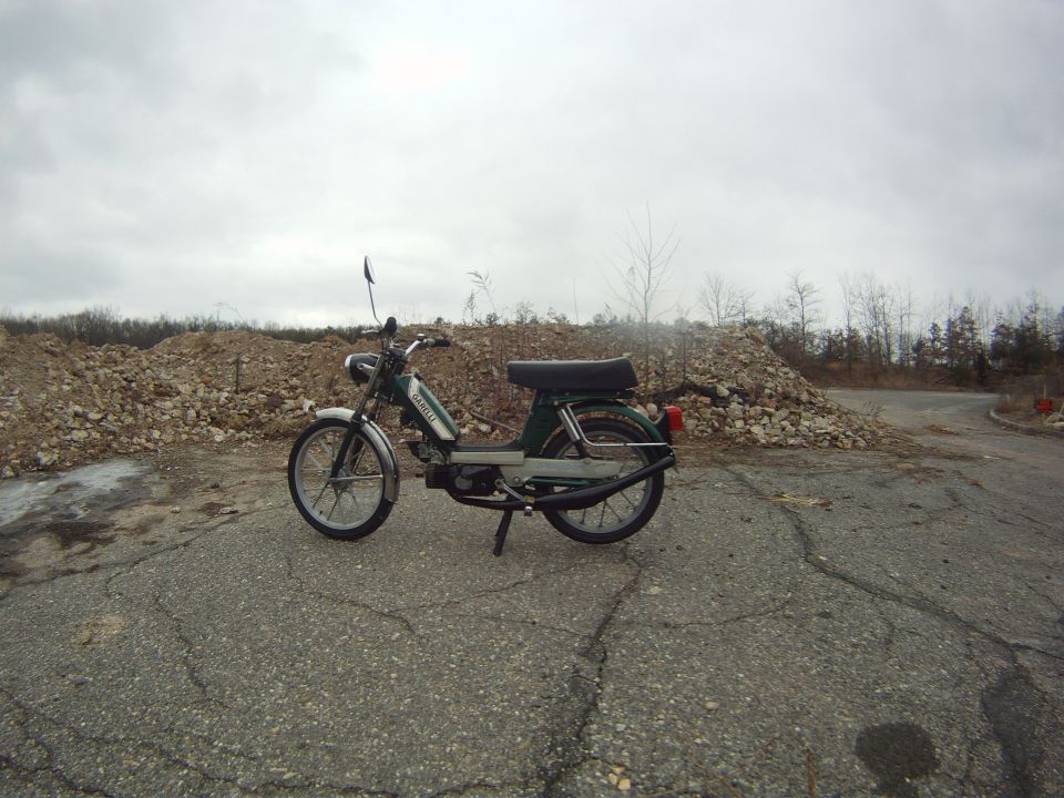 Green moped parked on cracked asphalt with piles of rubble in the background