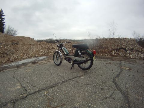 1981 Garelli Rally Sport - A green moped sits on a broken road, surrounded by large piles of debris under a cloudy sky.