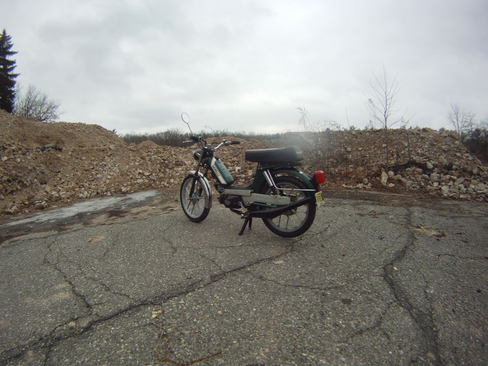 green moped parked on cracked asphalt with piles of rubble in background