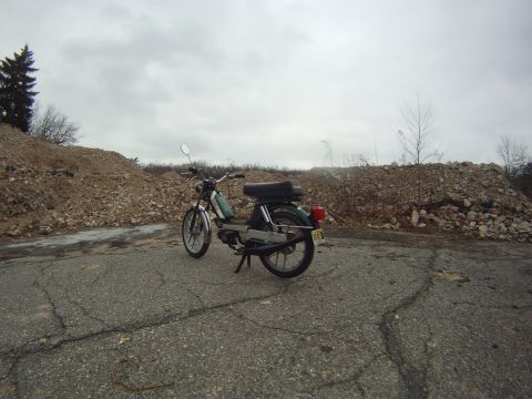 1981 Garelli Rally Sport - A moped is parked on a road with piles of rubble surrounding it under a cloudy sky.
