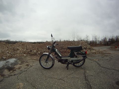 1981 Garelli Rally Sport - Green moped parked on cracked asphalt with piles of rocks and trees in the background.