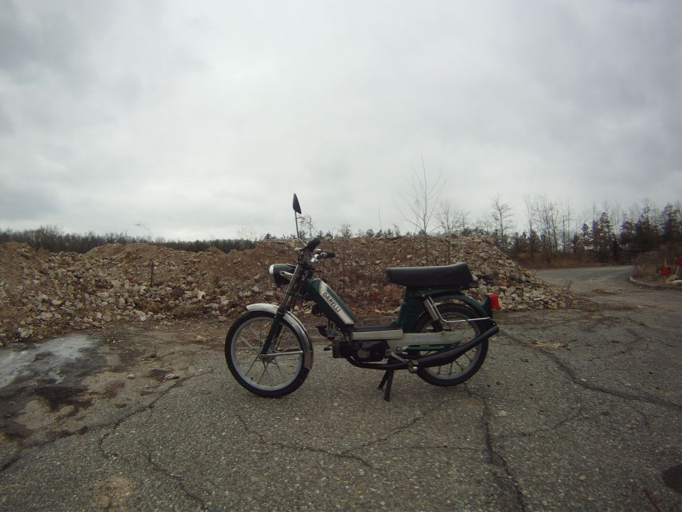 Green moped with 'GARELLI' text on the side, parked outdoors on cracked pavement with piles of rocks in the background