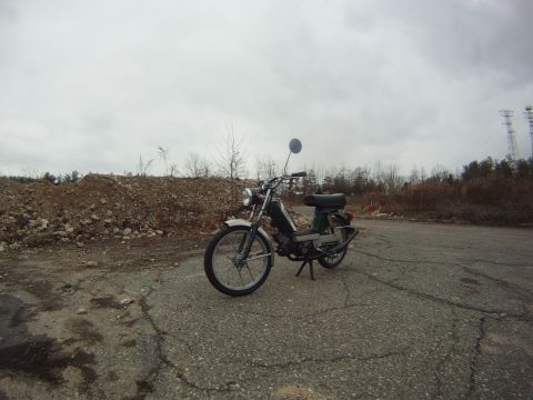 1981 Garelli Rally Sport - A moped sits parked on a desolate road under an overcast sky, with a large pile of rocks and sparse trees behind it.