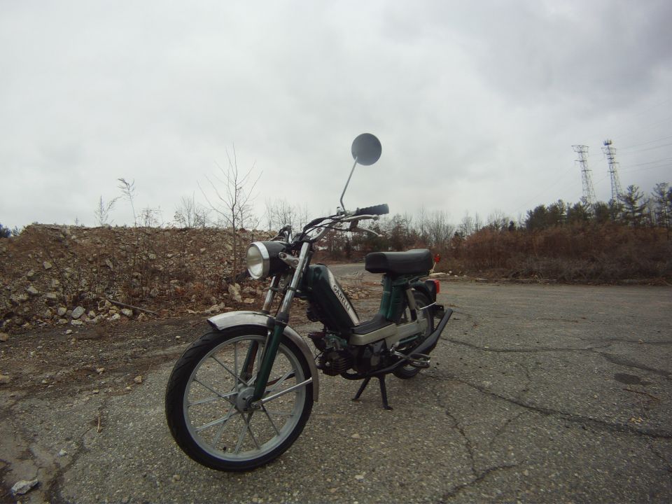 Green moped with chrome fender and round mirror parked on asphalt
