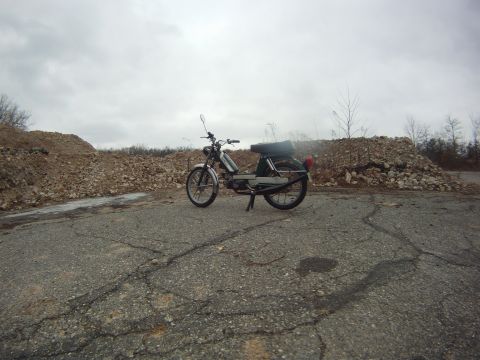 1981 Garelli Rally Sport - A moped sits on a desolate road, surrounded by large piles of construction debris under an overcast sky.