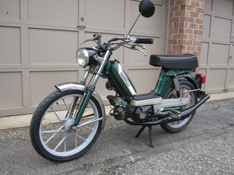 Green moped with 'GARELLI' text on the tank, parked in front of a garage