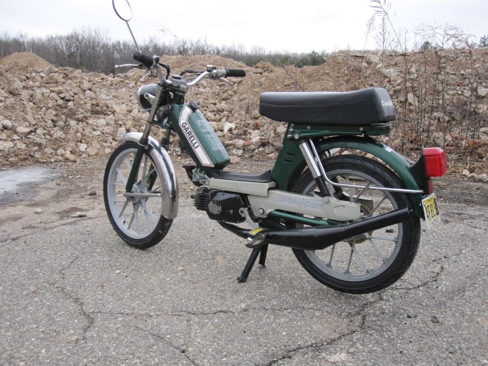 Green moped with chrome fenders and black seat parked on asphalt