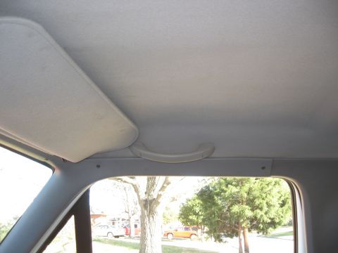 1994 Ford Bronco - Interior view of a car's ceiling, sun visor, and grab handle, with a glimpse of the outdoors including trees and other vehicles.
