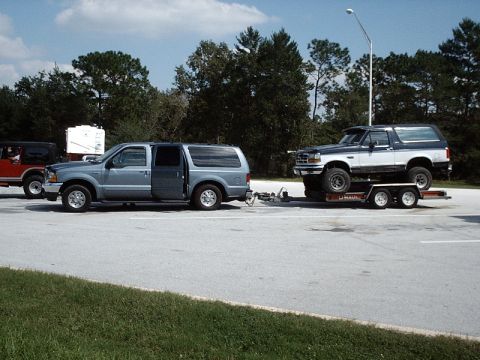 1996 Ford Bronco - A two-tone Ford Bronco is loaded onto a U-Haul trailer, with another SUV parked nearby.
