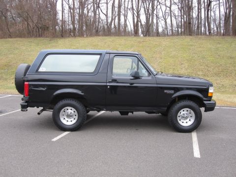 1996 Ford Bronco - A black 1996 Ford Bronco SUV is parked on an asphalt lot, viewed from the side with a spare tire mounted on the rear.
