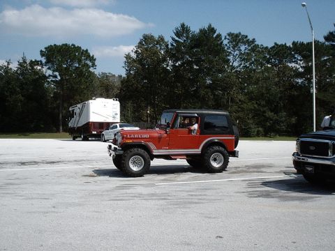 1996 Ford Bronco - A red Jeep CJ7 Laredo is parked next to a large RV and a dark pickup truck.