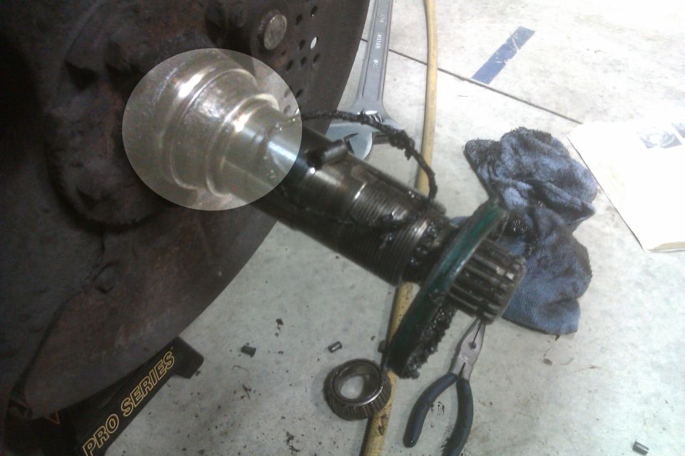 Greasy spindle and hub on a rusty rotor with wheel bearing, pliers, and rag on shop floor