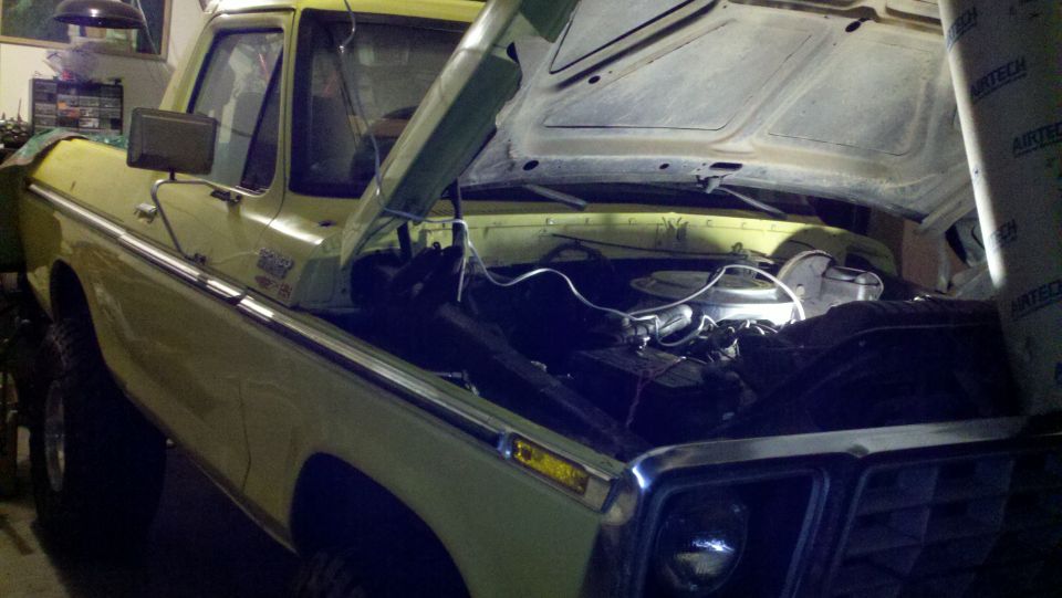 Yellow Ford truck, front quarter view, hood open showing engine compartment. Chrome trim and side molding visible